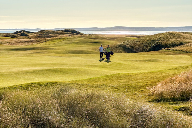 A man tee-ing off with Another Place, The Machrie in the background