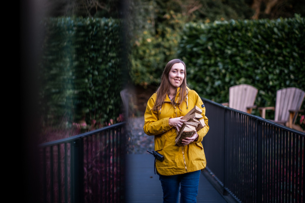 Lady in a yellow coat carrying wood for a log burner 