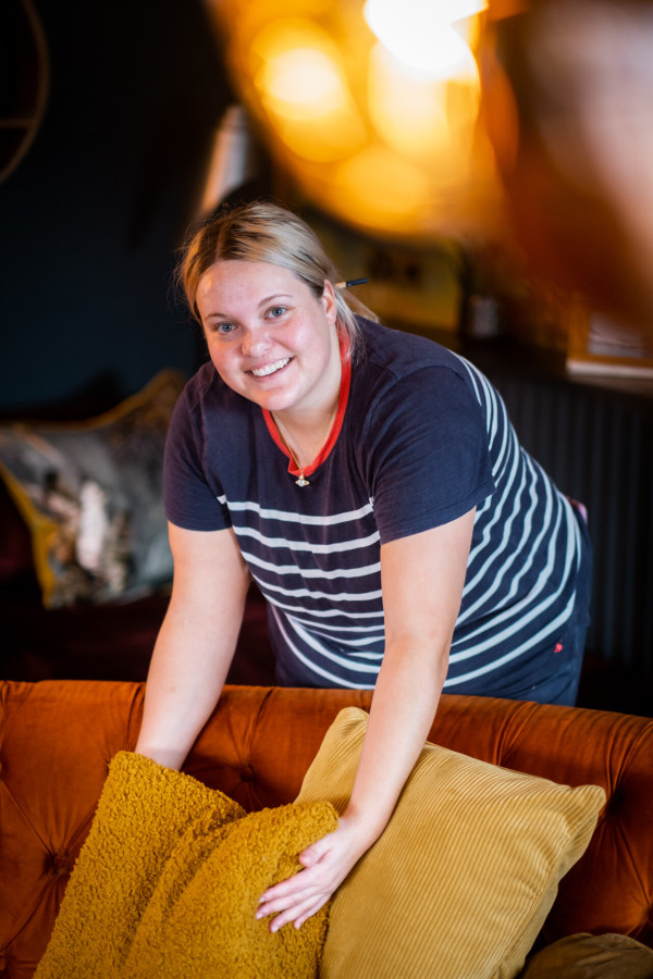 Housekeeper straightening pillows on a sofa
