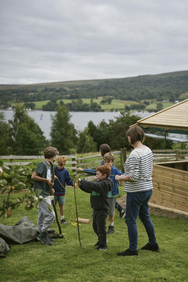 Lady helping children at a forest school at Another Place, The Lake