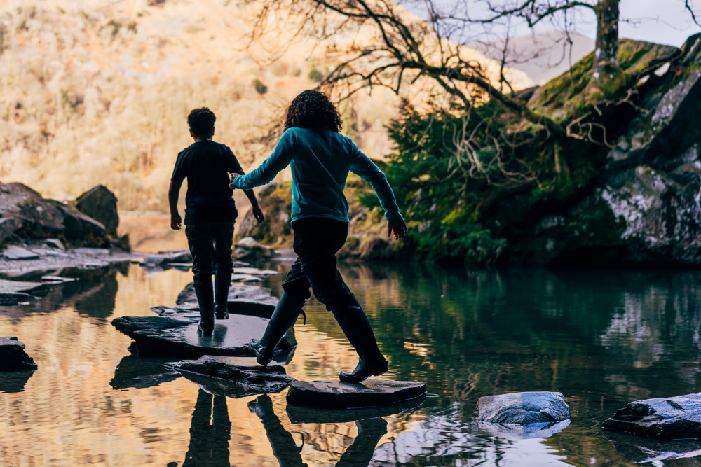 People walking across stepping stones wearing Warm Welly Company wellies