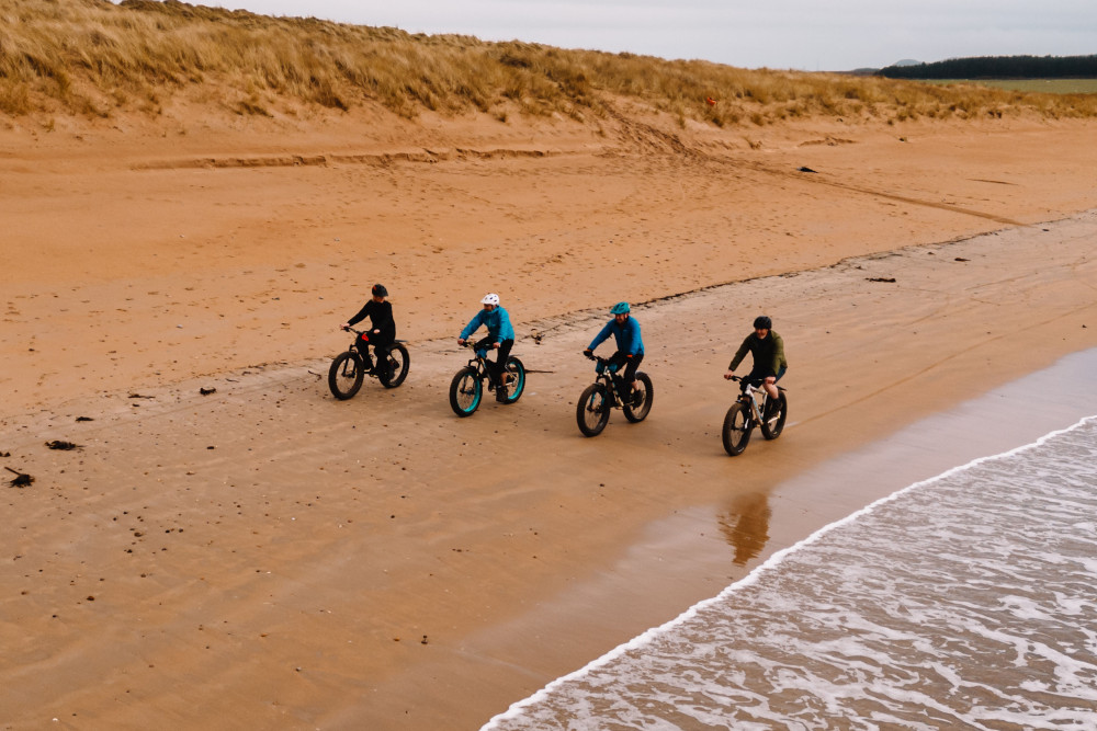 Four people fatbiking on the beach by Another Place, The Machrie