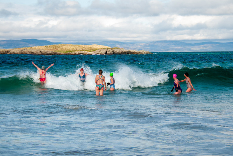Group of women in swimsuits jumping over waves on the coast of islay