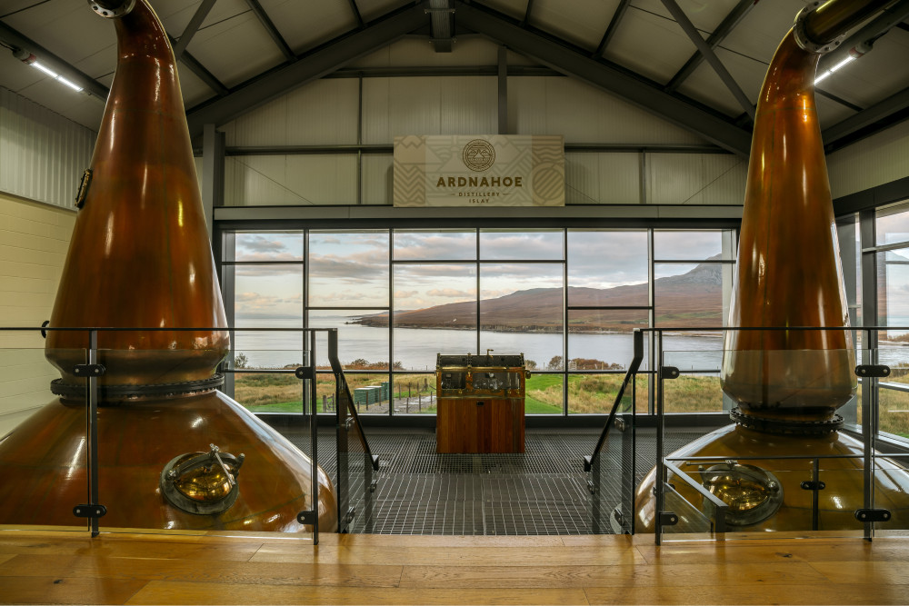 An image from the inside looking out of Ardnahoe distillery nestled next to Ardnahoe loch, Paps of Jura in the background