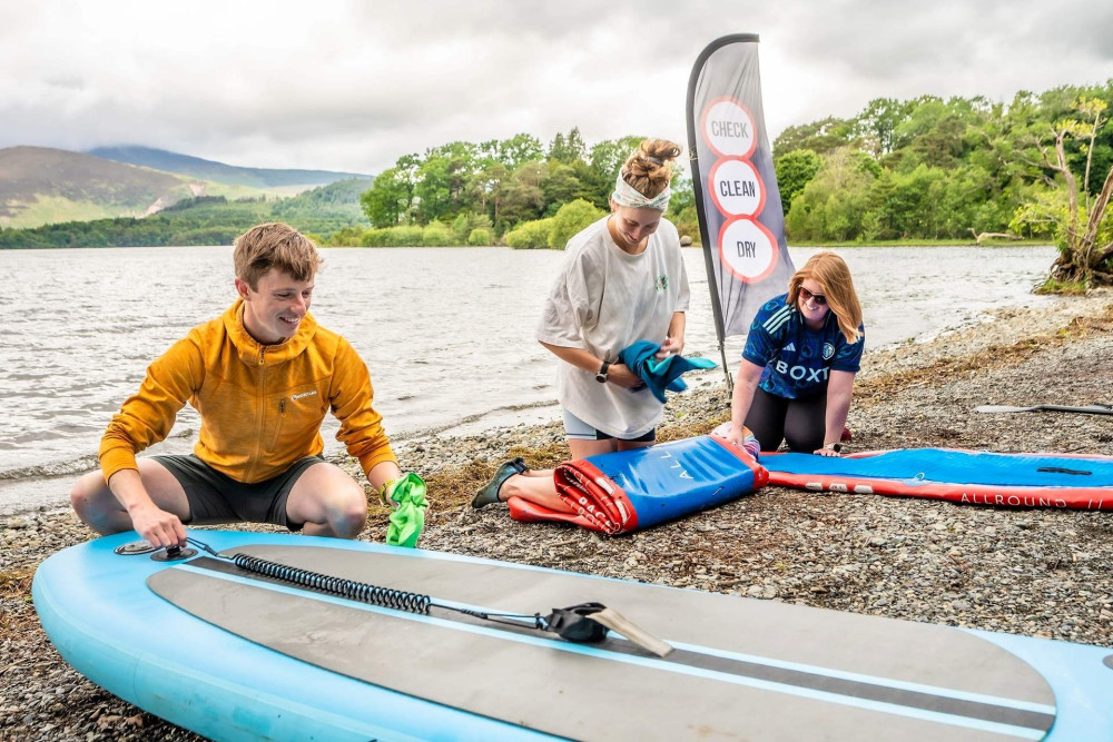 Two women and a man rolling out and inflating paddleboards on the lake shore