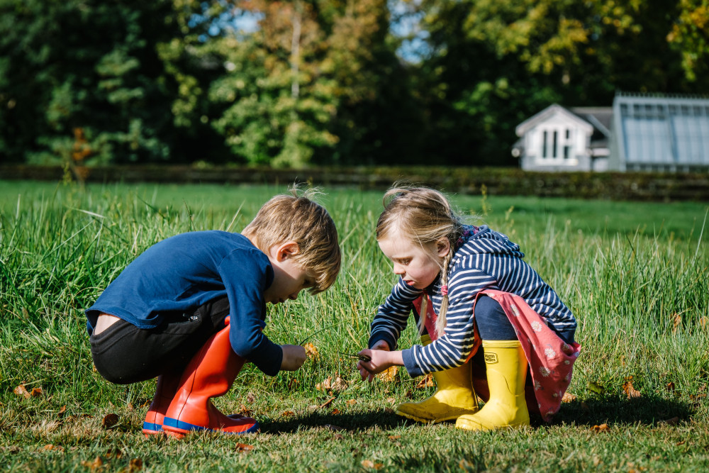 Two children crouching searching through the grass wearing wellies